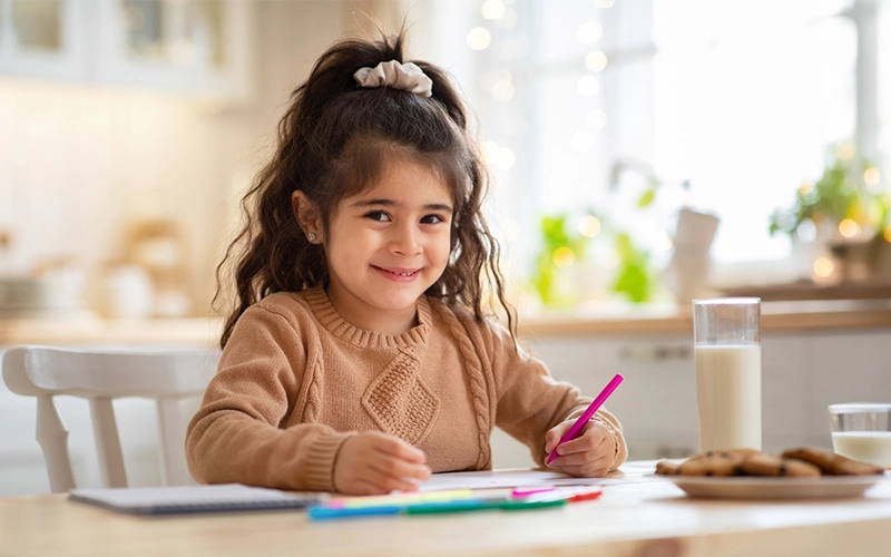 Criança sorridente desenhando em uma mesa